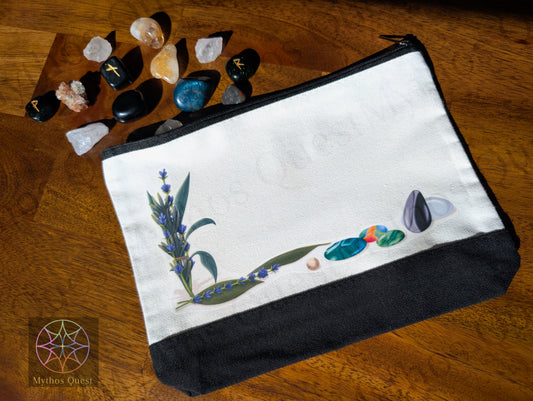 White pouch with nature themed design on a wooden surface with gems and Nordic ruins. Company logo on the bottom left.
